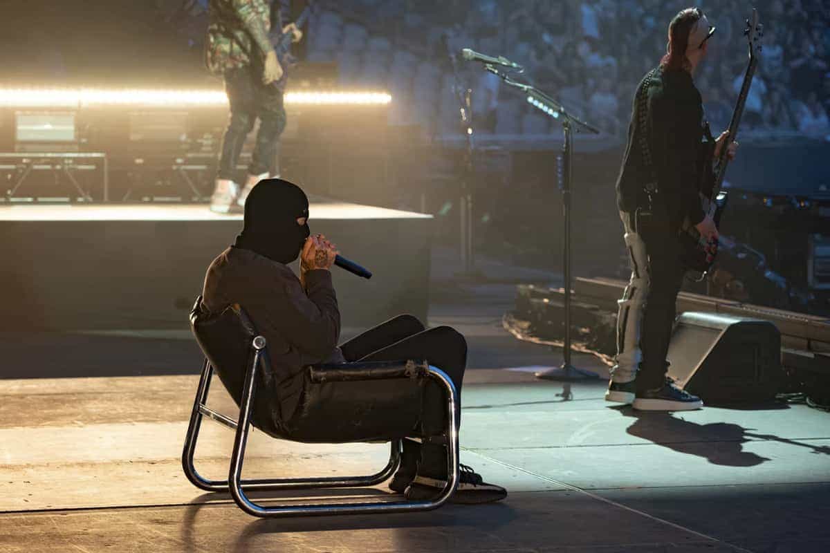 Avenged Sevenfold singer sitting in chair on stage wearing a balaclava